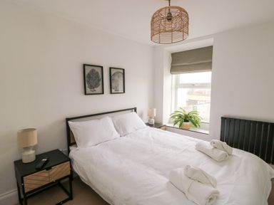 A bedroom with a double bed white bedding bedside tables with lamps a window with a plant and wall art above the bed at 1 Mona Terrace in Llanfachraeth