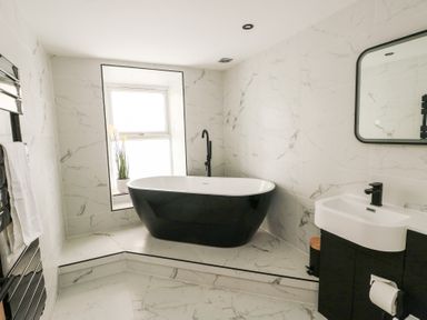 A bathroom with a black freestanding bathtub near a window and a sink with a mirror at 1 Mona Terrace in Llanfachraeth