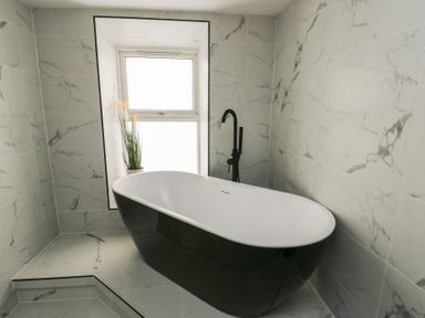 A bathroom with a black and white freestanding bathtub near a window with a plant at 1 Mona Terrace in Llanfachraeth