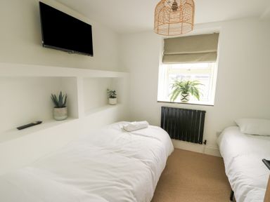 A bedroom with two single beds a mounted television and plants on shelves and window at 1 Mona Terrace in Llanfachraeth