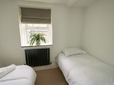 A small bedroom with two single beds a window with a plant on the sill and a black radiator at 1 Mona Terrace in Llanfachraeth