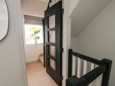 A stair landing area with a black door and a window with a potted plant at 1 Mona Terrace in Llanfachraeth