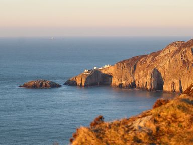 A coastal cliff with buildings on top overlooking the sea at 1 Mona Terrace in Llanfachraeth