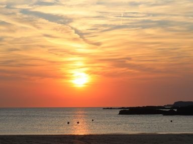 A sunset over the ocean with a partially cloudy sky and rocky coastline at 1 Mona Terrace in Llanfachraeth