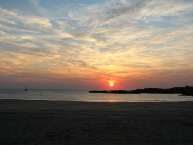 A sunset over the ocean with a sandy beach in the foreground and a sailboat in the distance at 1 Mona Terrace in Llanfachraeth
