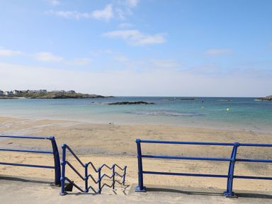 A sandy beach with blue railings and stairs leading to the shore at 1 Mona Terrace in Llanfachraeth