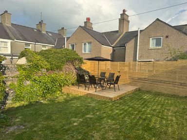 A backyard with a wooden deck and outdoor table with six chairs and an umbrella at 1 Mona Terrace in Llanfachraeth