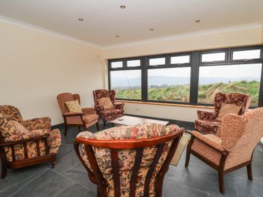A sitting room with six upholstered armchairs around a wooden coffee table and large windows showing grass outside at Castell Y Garn near Newport Beach Pembrokeshire