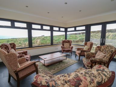 A sitting room with six armchairs around a coffee table and large windows showing grass at Castell Y Garn near Newport Beach Pembrokeshire