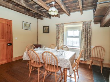 A dining room with a wooden table covered by a tablecloth and six wooden chairs under a wooden beam ceiling at Castell Y Garn near Newport Beach Pembrokeshire