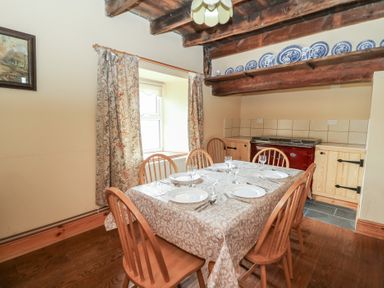 A dining room with a wooden table set for six and wooden chairs near a window and kitchen area at Castell Y Garn near Newport Beach Pembrokeshire