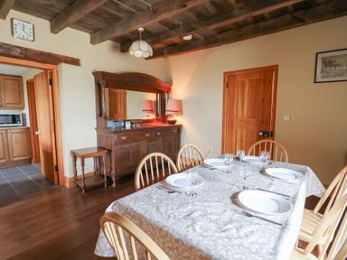 A dining room with a wooden table set with plates and glasses and a wooden sideboard at Castell Y Garn near Newport Beach Pembrokeshire