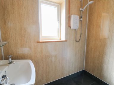 A bathroom with a white sink and a shower unit mounted on the wall near a window at Castell Y Garn near Newport Beach Pembrokeshire