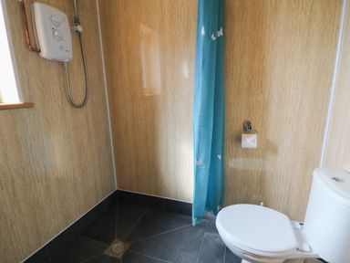 A bathroom with a toilet a blue shower curtain and a shower unit on the wall at Castell Y Garn near Newport Beach Pembrokeshire