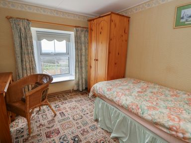 A bedroom with a single bed a wooden wardrobe a wooden desk a wicker chair and a window at Castell Y Garn near Newport Beach Pembrokeshire
