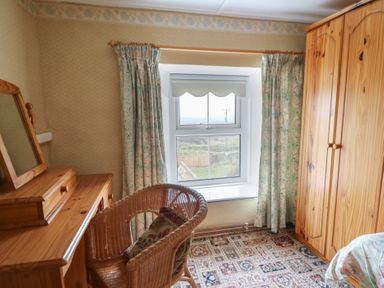 A bedroom corner with wooden wardrobe and dressing table a wicker chair and a window with curtains at Castell Y Garn near Newport Beach Pembrokeshire