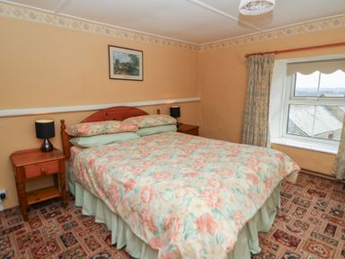 A bedroom with a floral bedspread two bedside tables with lamps a window and patterned carpet at Castell Y Garn near Newport Beach Pembrokeshire