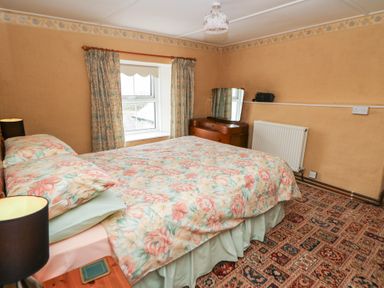 A bedroom with a double bed with floral bedding a window with curtains a wooden dresser with a mirror and a patterned carpet at Castell Y Garn near Newport Beach Pembrokeshire