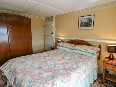 A bedroom with a floral bedspread a wooden wardrobe a nightstand with a lamp and a framed picture on the wall at Castell Y Garn near Newport Beach Pembrokeshire