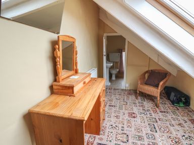 A room with a wooden vanity desk with a mirror a wicker chair and a bathroom door under a slanted ceiling at Castell Y Garn near Newport Beach Pembrokeshire