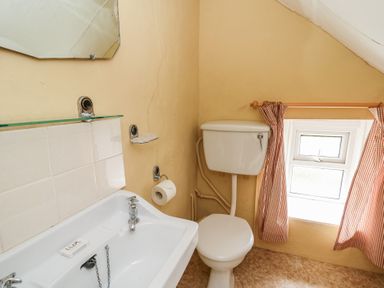 A small bathroom with a white sink and toilet next to a window with red checked curtains at Castell Y Garn near Newport Beach Pembrokeshire