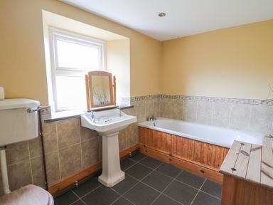 A bathroom with a bathtub sink toilet and a wooden cabinet near a window at Castell Y Garn near Newport Beach Pembrokeshire