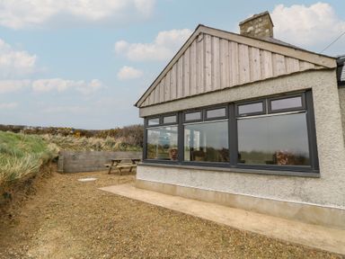 The exterior side view of a house with large windows and a wooden picnic table on gravel near grass at Castell Y Garn near Newport Beach Pembrokeshire