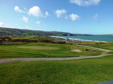 A golf course by the coastline with a path and hills in the background near Newport Beach Pembrokeshire