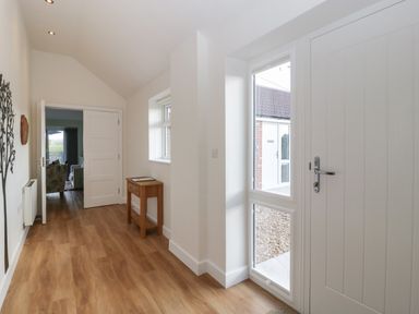 An entryway with wooden flooring a small wooden table a white door and a wall decoration at Doubletree Cottage in Swainsford near Mere