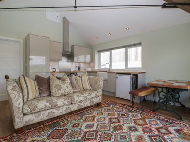 A living room with a patterned sofa and colorful rug next to a kitchen with cabinets and a dining table at Doubletree Cottage in Swainsford near Mere