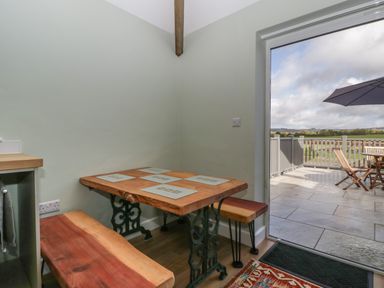 A corner dining area with a wooden table and benches next to a glass door leading to a patio with outdoor furniture at Doubletree Cottage in Swainsford near Mere