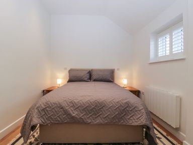 A bedroom with a double bed with two pillows and a quilt two bedside tables with lamps a small window with shutters and a radiator on the wall at Doubletree Cottage in Swainsford near Mere