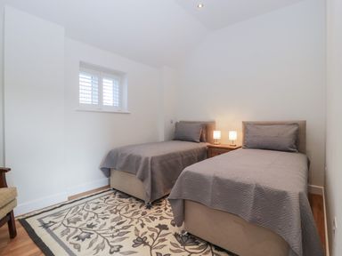 A bedroom with two single beds a small wooden nightstand with lamps and a patterned rug at Doubletree Cottage in Swainsford near Mere