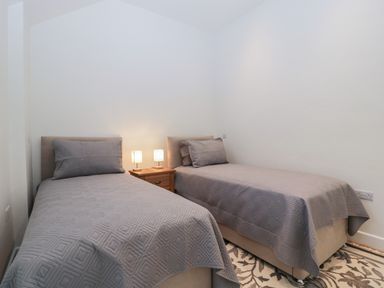 A bedroom with two single beds covered in gray bedspreads and a wooden nightstand with two lamps at Doubletree Cottage in Swainsford near Mere