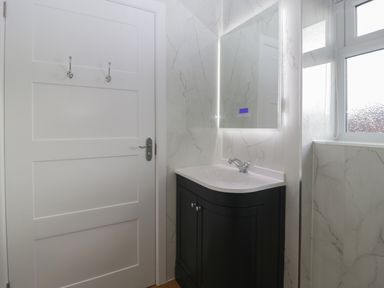 A bathroom sink with a black cabinet and illuminated mirror next to a white door and window at Doubletree Cottage in Swainsford near Mere