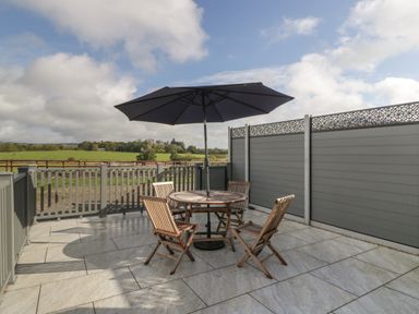 An outdoor patio with a round table four wooden chairs and a large umbrella overlooking green fields at Doubletree Cottage in Swainsford near Mere