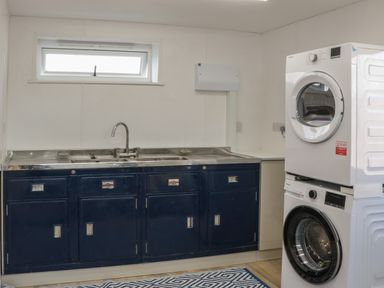 A laundry room with a stacked washer and dryer and blue cabinets with a sink at Doubletree Cottage in Swainsford near Mere