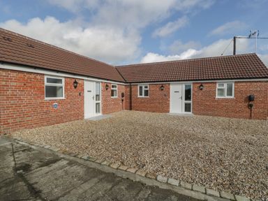 A courtyard with gravel and two brick buildings with tiled roofs and white doors at Singletree Cottage in Swainsford near Mere