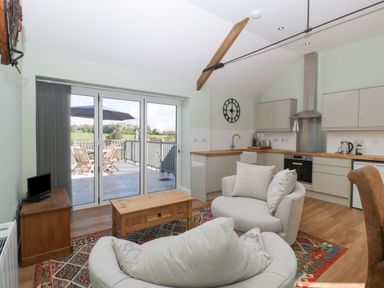 A kitchen and living area with armchairs a wooden coffee table a television and glass doors leading to an outdoor patio at Singletree Cottage in Swainsford near Mere