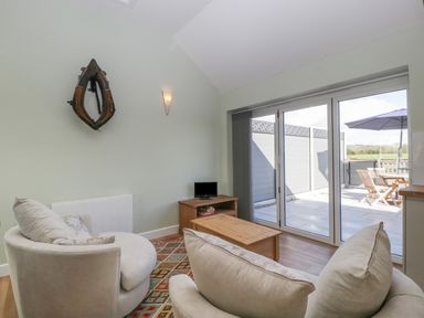 A living room with two beige armchairs a wooden coffee table a small TV on a wooden stand a patterned rug and sliding glass doors to a patio at Singletree Cottage in Swainsford near Mere