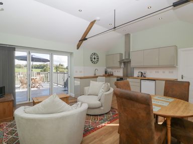 An open-plan kitchen and living area with armchairs a round dining table and kitchen cabinets at Singletree Cottage in Swainsford near Mere