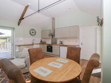 A kitchen and dining area with round wooden table and brown chairs at Singletree Cottage in Swainsford near Mere
