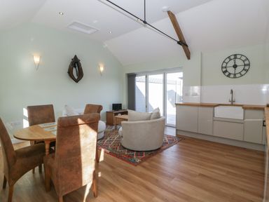 An open plan living and kitchen area with round dining table chairs sofa coffee table wall clock and sliding glass doors at Singletree Cottage in Swainsford near Mere
