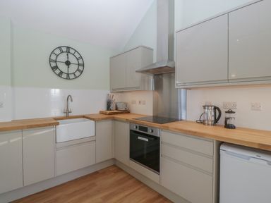 A kitchen with wooden countertops cabinets a wall clock and appliances at Singletree Cottage in Swainsford near Mere