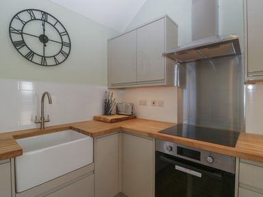 A kitchen corner with a farmhouse sink wooden countertops a stove with stainless steel hood knives in a block and a wall clock at Singletree Cottage in Swainsford near Mere