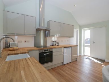 A kitchen with wooden countertops gray cabinets an oven a sink and a door with windows at Singletree Cottage in Swainsford near Mere