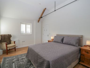 A bedroom with a bed two bedside tables with lamps an armchair and a window with shutters at Singletree Cottage in Swainsford near Mere