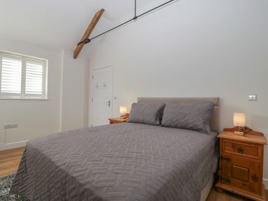 A bedroom with a bed with gray bedding and wooden bedside tables with lamps at Singletree Cottage in Swainsford near Mere