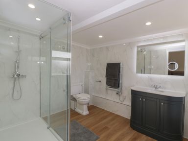A bathroom with a glass shower, toilet, heated towel rail, dark vanity cabinet with sink and illuminated mirror at Singletree Cottage in Swainsford near Mere