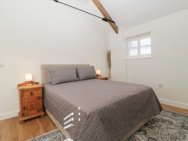 A bedroom with a bed covered in a gray quilt and wooden bedside tables with lamps at Singletree Cottage in Swainsford near Mere